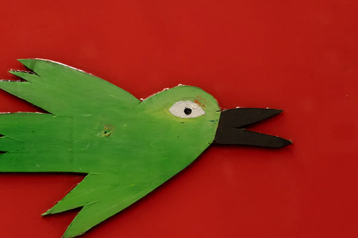 Detail of a green cardboard bird mounted proud of the red ground