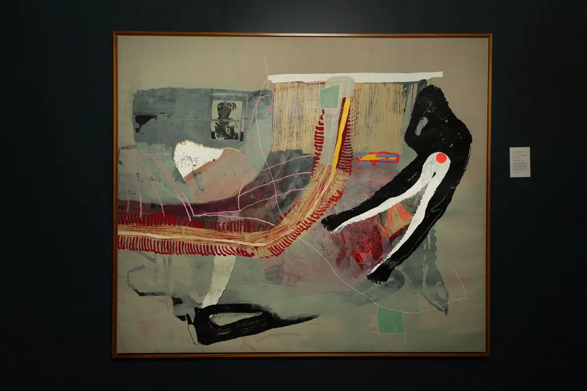 The framed work on a dark wall at TolHouse beside its wall label