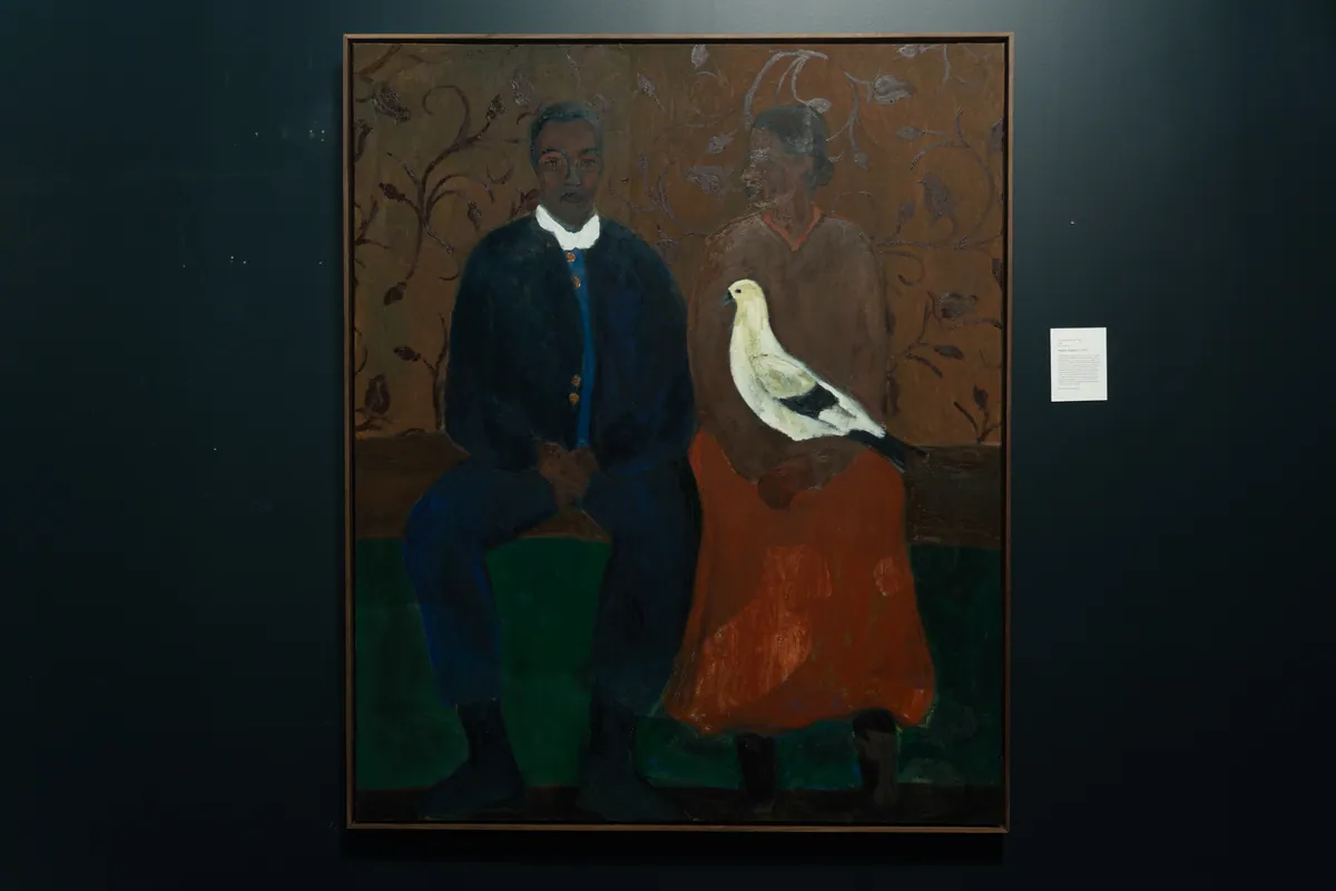 The framed painting on a dark wall at TolHouse beside its wall label